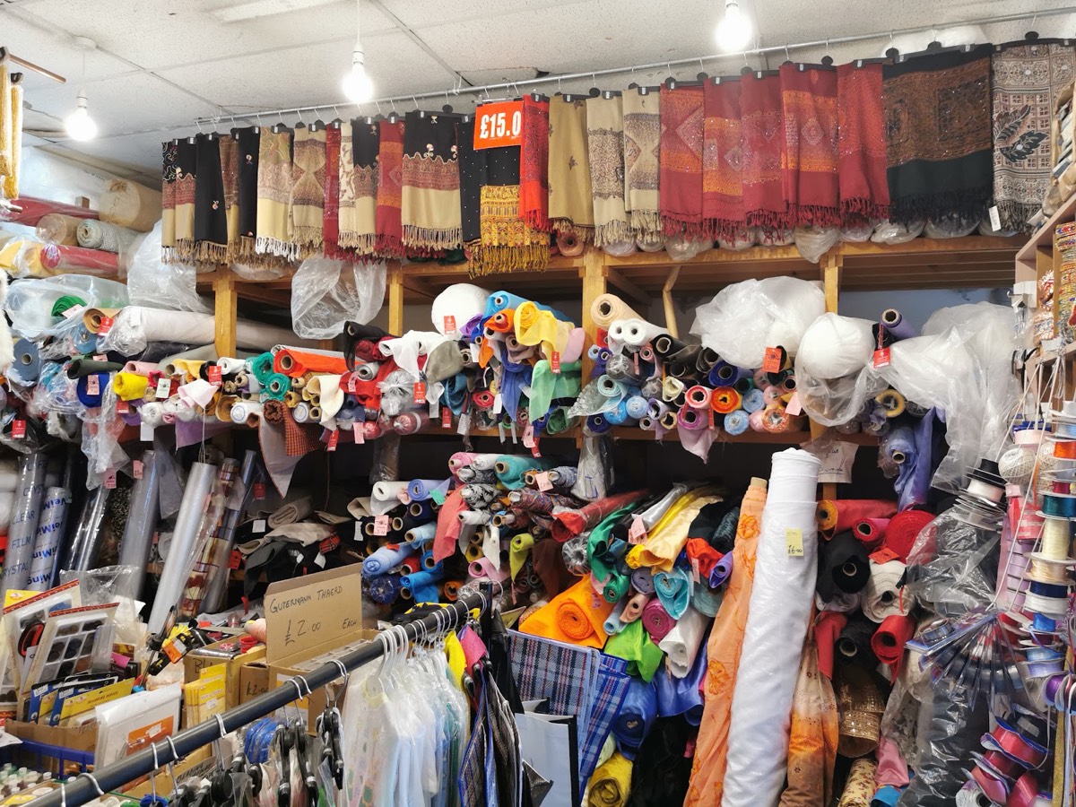 Shelves of fabric rolls with a row of embroidered pashmina shawls hung above at Z. Butt Textiles, Brick Lane.
